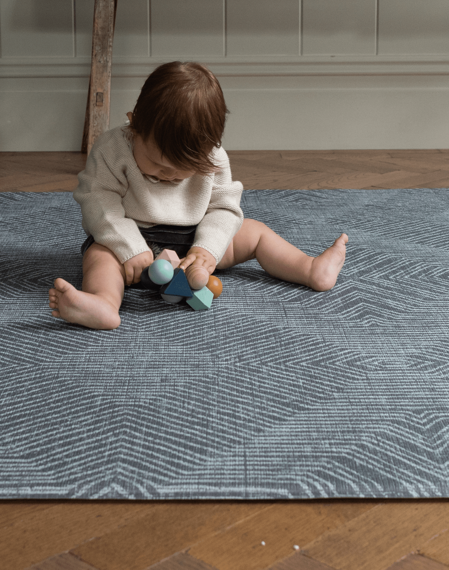 Baby girl plays with a wooden baby toy supported on the eclipse monochrome play mat that provides protection from the cold floor