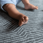 Baby feet are supported on the grijs speelmat designed from birth to keep floor play protected and safe
