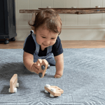 Baby crawls across a textile inspired floor mat  playing with a trio of wooden play cars perfect for baby floor play