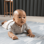Baby enjoying tummy time on Large round play mat by Totter and Tumble acts like a wipeable rug in the family home easy to clean spit up and spillages and looks stylish
