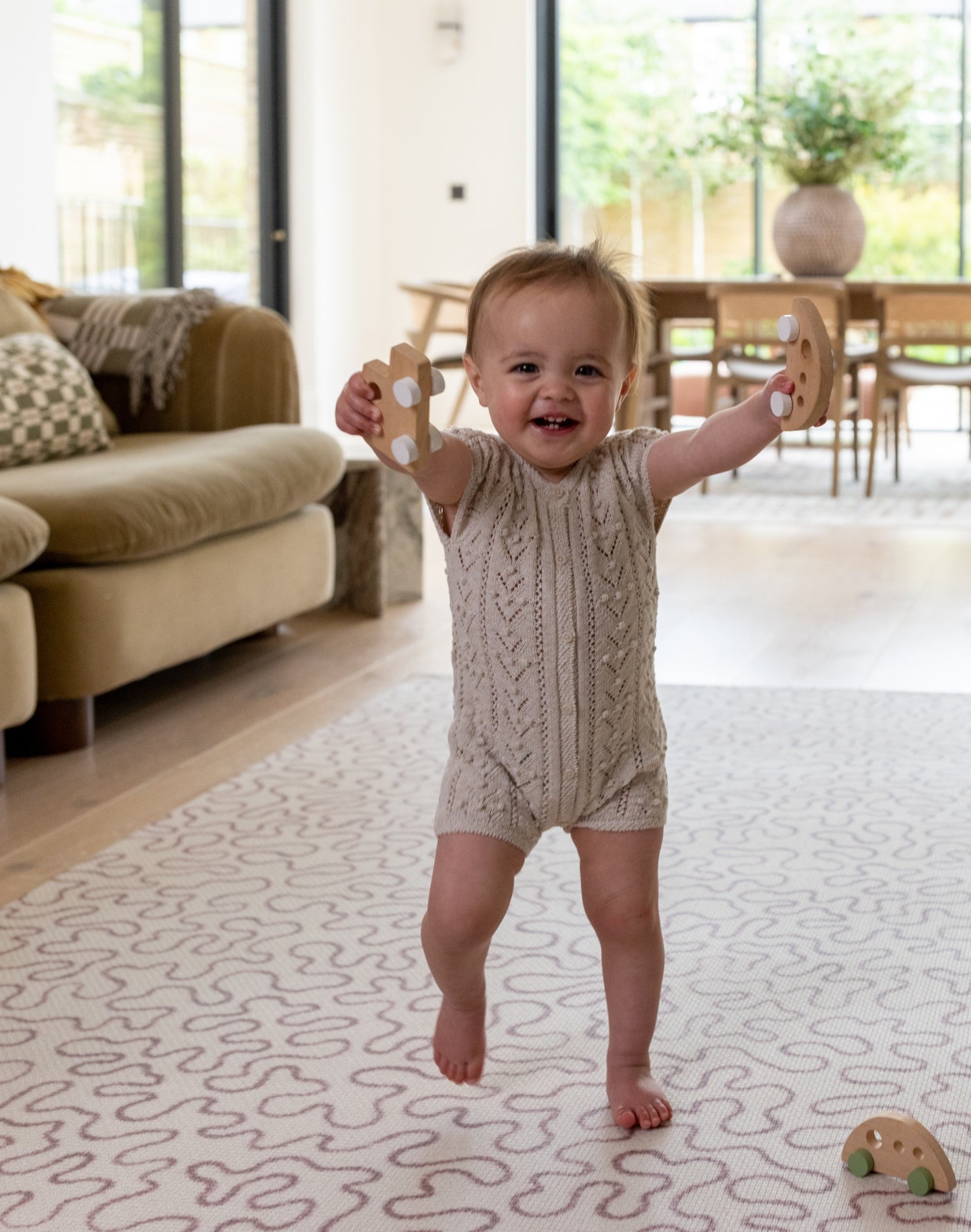 Toddler playing on The Brecon, a large play mat for crawling baby and walking toddler in a neurtal red colour palette