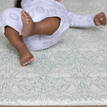 Little baby feet on a soft playmat in a subtle sage green William Morris design.