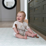 Toddler sits comfortably on The Brer Rabbit Playmat in the kitchen. The playmat is a stylish baby essential that blends designer nursery decor with practical, non-toxic materials.