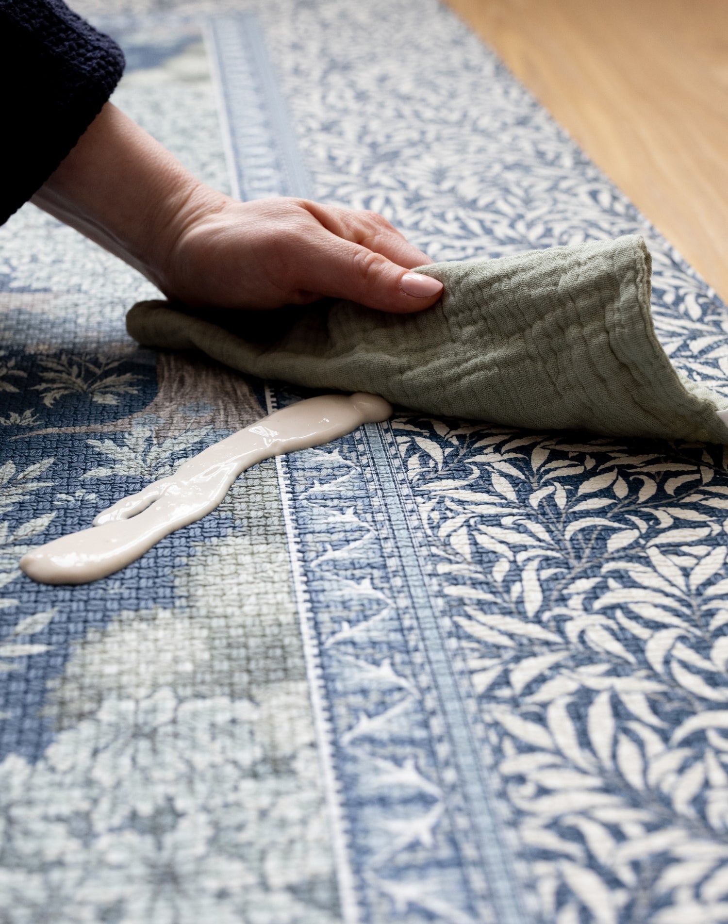 Detailed view of the durable Totter + Tumble nursery Brook play mat. A muslin cloth wipes up a spill on the playmat with ease