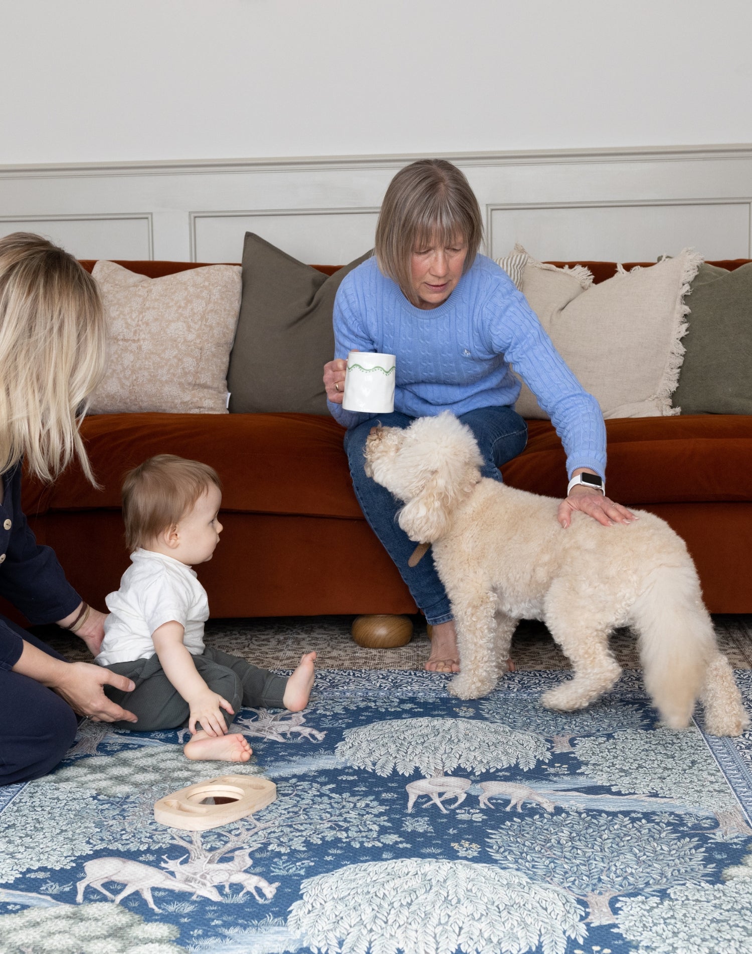 Stylish family room with baby, mum, grandma and dog playing on a Totter + Tumble playmat - a family-friendly interior item.