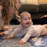 Baby smiling on a safe, non-toxic foam playmat with classic woodland prints from Totter + Tumble x Morris & Co. collection.