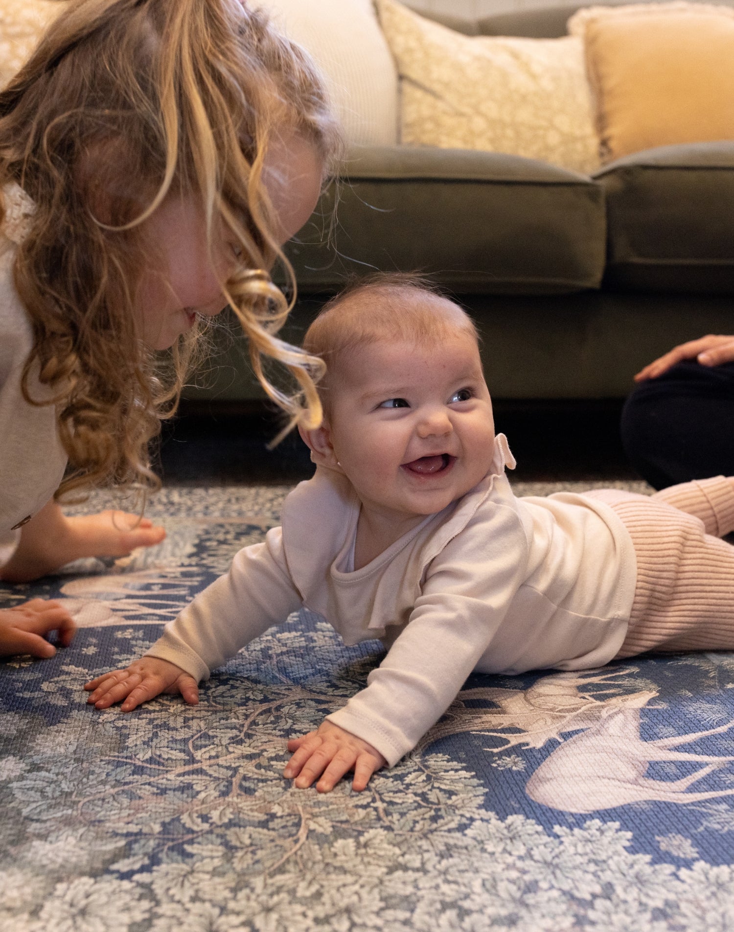 Baby smiling on a safe, non-toxic foam playmat with classic woodland prints from Totter + Tumble x Morris & Co. collection.