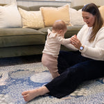 Parent supports standing baby on a luxury nursery play mat in warm woodland hues - a timeless, practical yet stylish baby mat