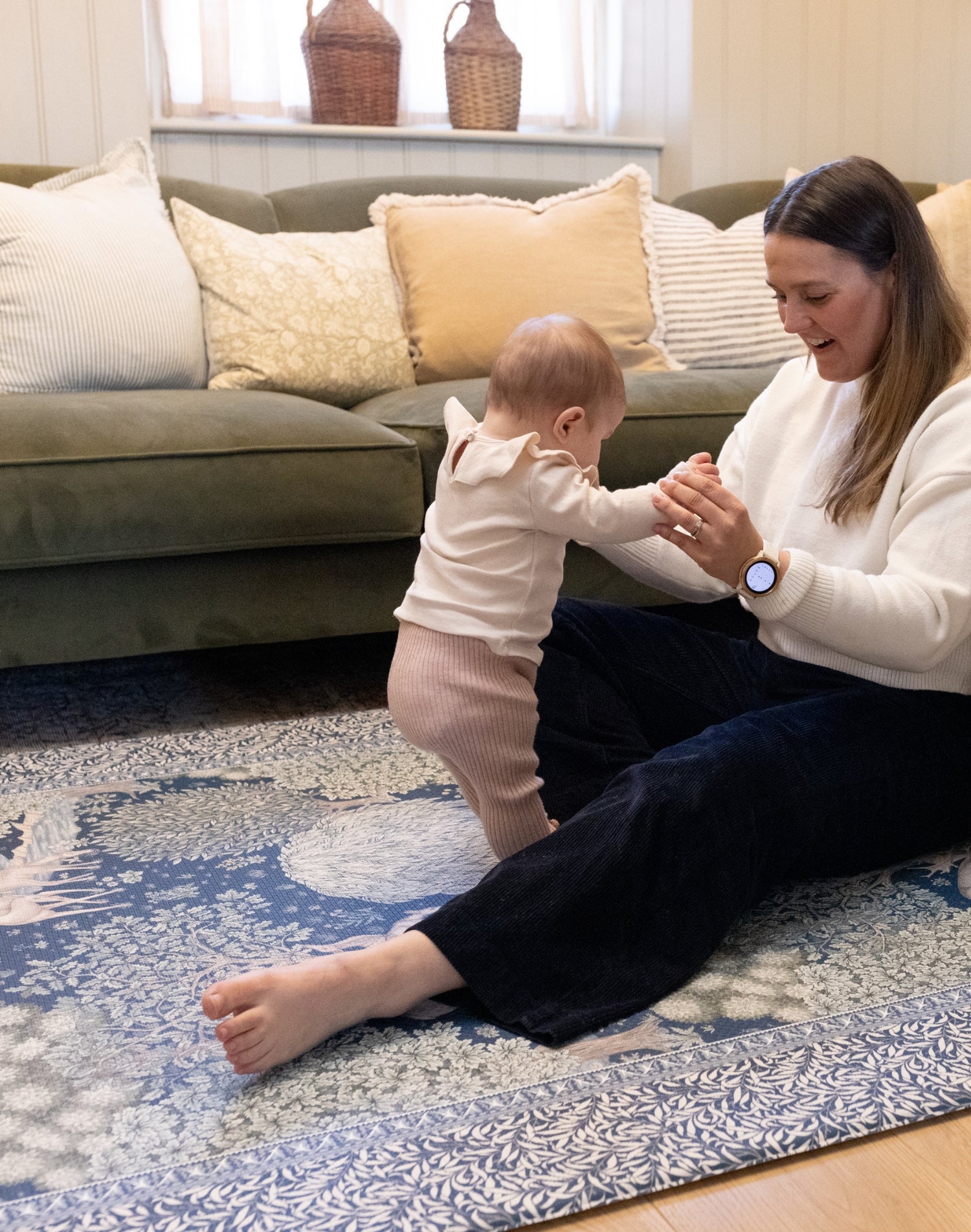 Parent supports standing baby on a luxury nursery play mat in warm woodland hues - a timeless, practical yet stylish baby mat