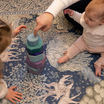 Children play with wooden stacking toys on a botanical-patterned play mat by Totter + Tumble. Safe play on a designer rug.
