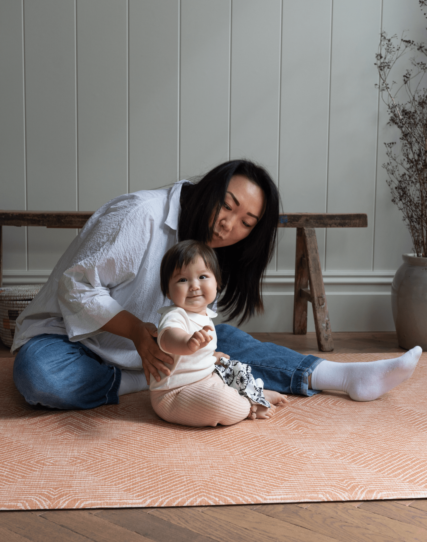 Baby and lady sit comfortably on thickly padded play mat with a modern kilim design