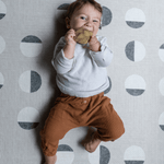 Baby boy chews on teether while relaxing on modern one piece practical play mat