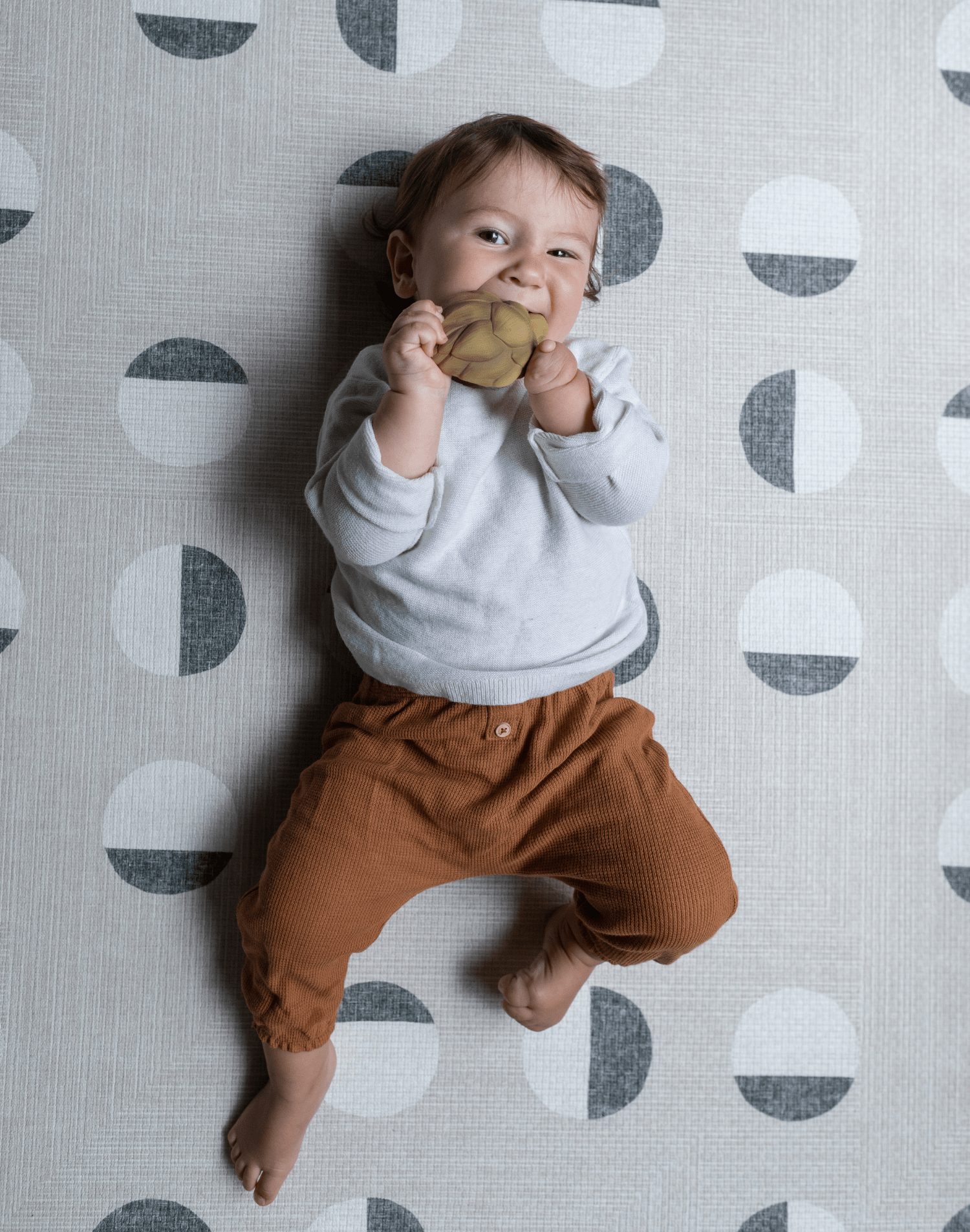 Baby boy chews on teether while relaxing on modern one piece practical play mat
