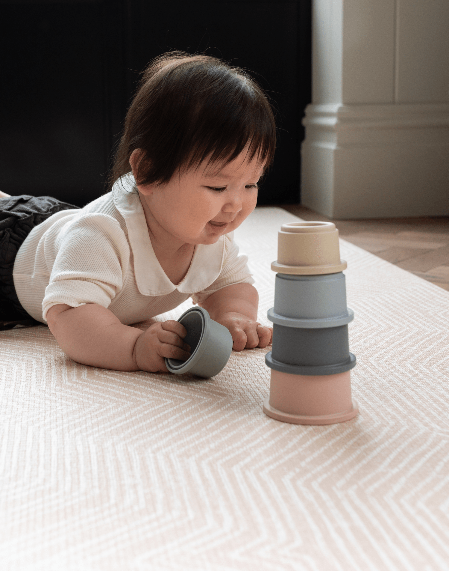 Little girl enjoys floor play with stacking cups on roze speelmat with gentle kilim textile design