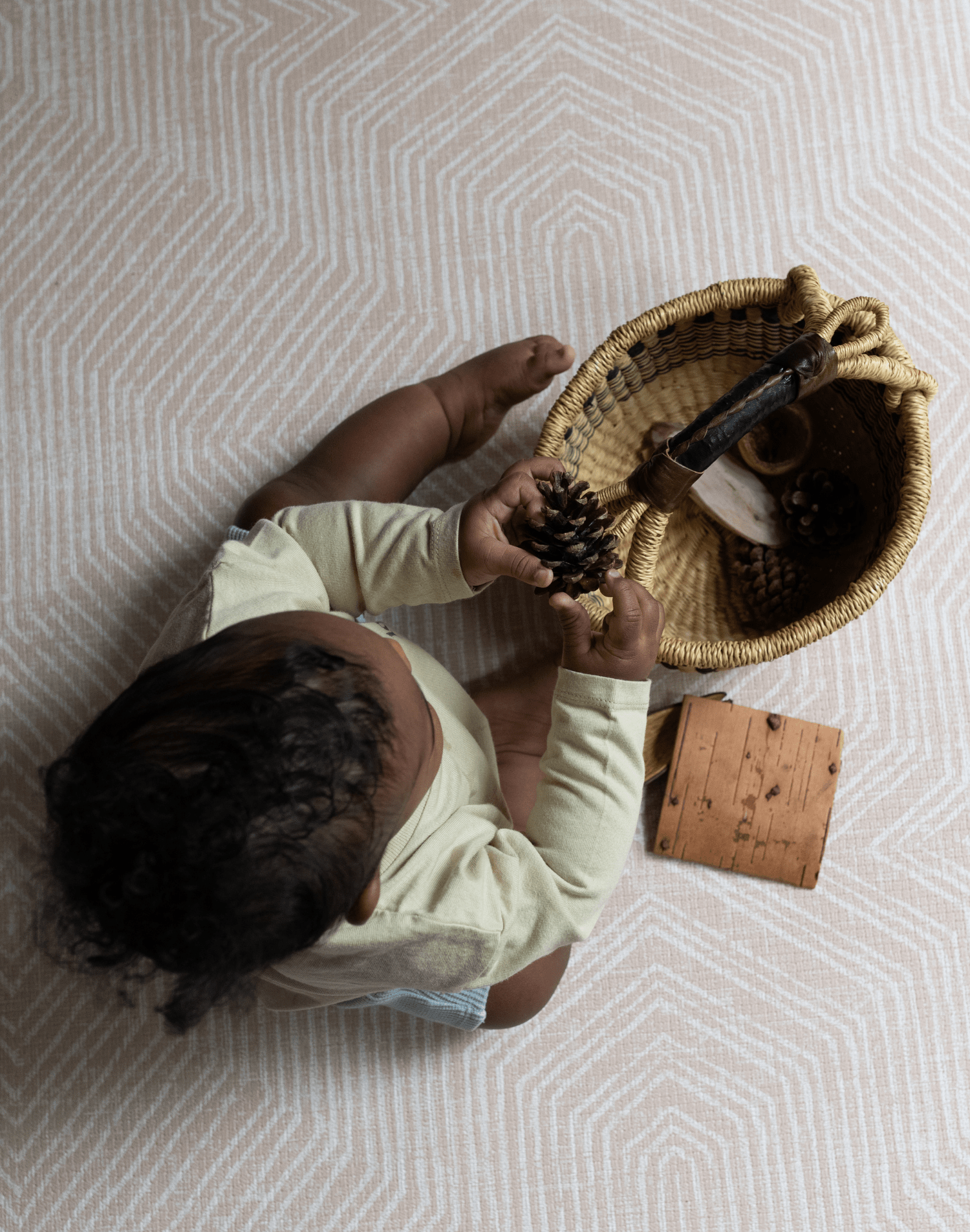 Little boy explores natural sensory basket for stimulation with thickly padded baby mat for a safe surface underneath