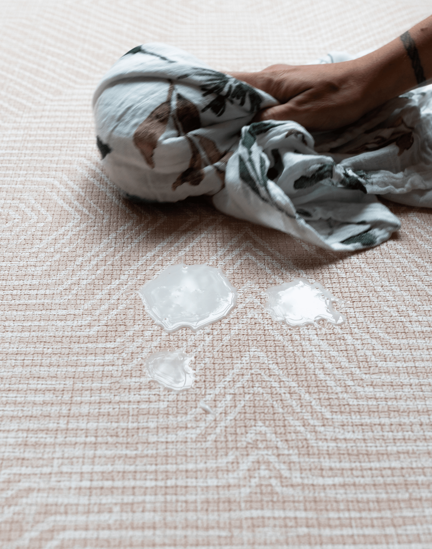 Wiping up milk with muslin on waterproof baby playmat