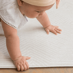 Little girl crawls across the Globe Trotter neutral play mat with a spongy surface that protects on hard wood flooring