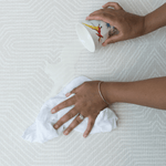 Hands wipe up a milk spill on the neutral play mat Globe Trotter  with a washable surface