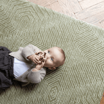 Baby is supported during play on the olive green play mat by Totter and Tumble with a decorative kilim effect