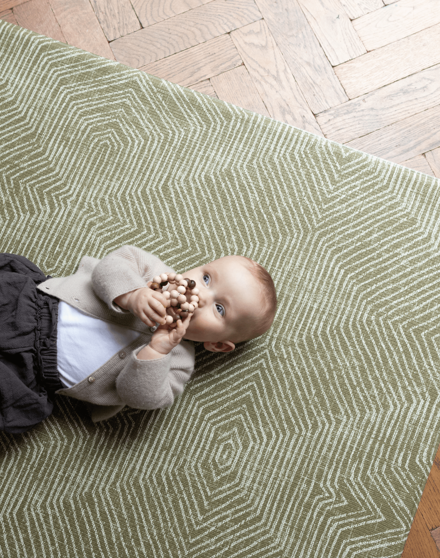 Baby is supported during play on the olive green play mat by Totter and Tumble with a decorative kilim effect