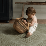 Baby plays with a basket sitting on the Harvester green baby mat that looks stylish in modern homes
