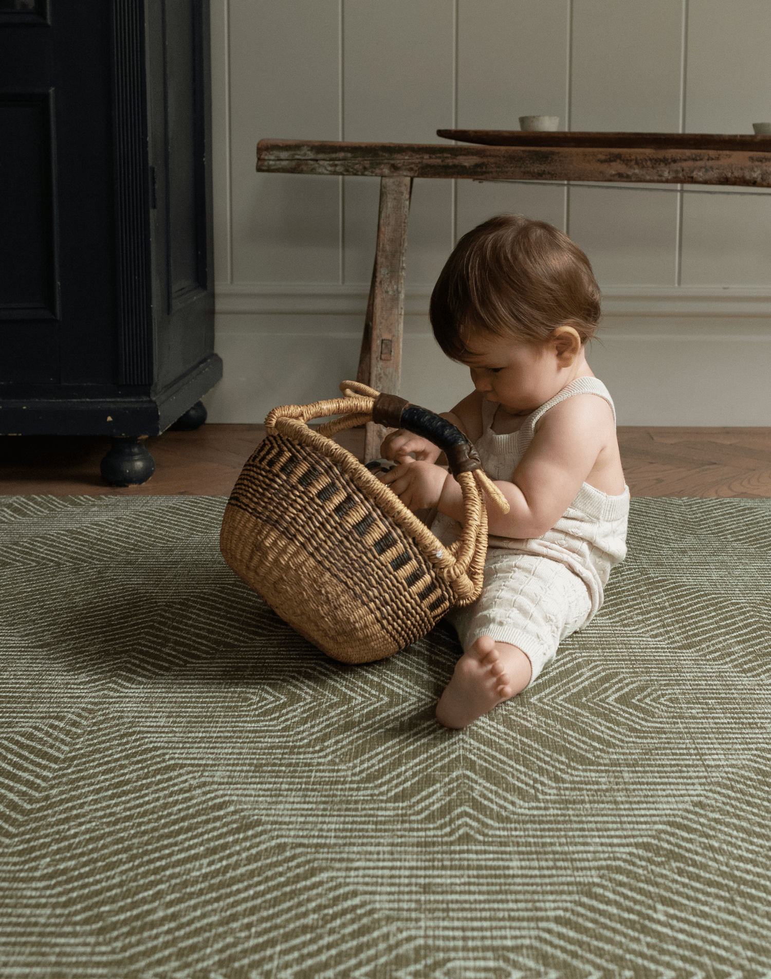 Baby plays with a basket sitting on the Harvester green baby mat that looks stylish in modern homes