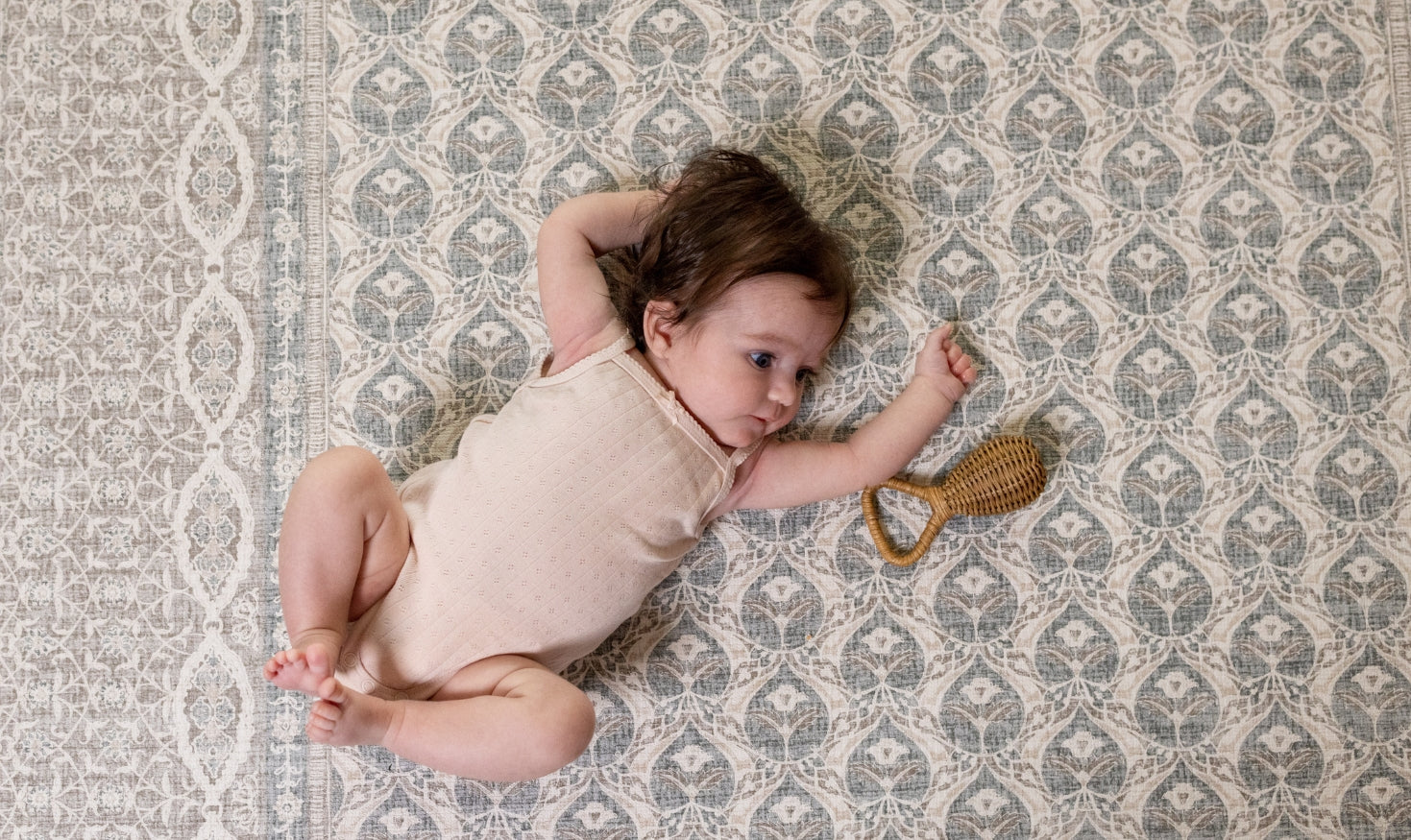 Baby lying on a patterned rug playmat with a rattle toy