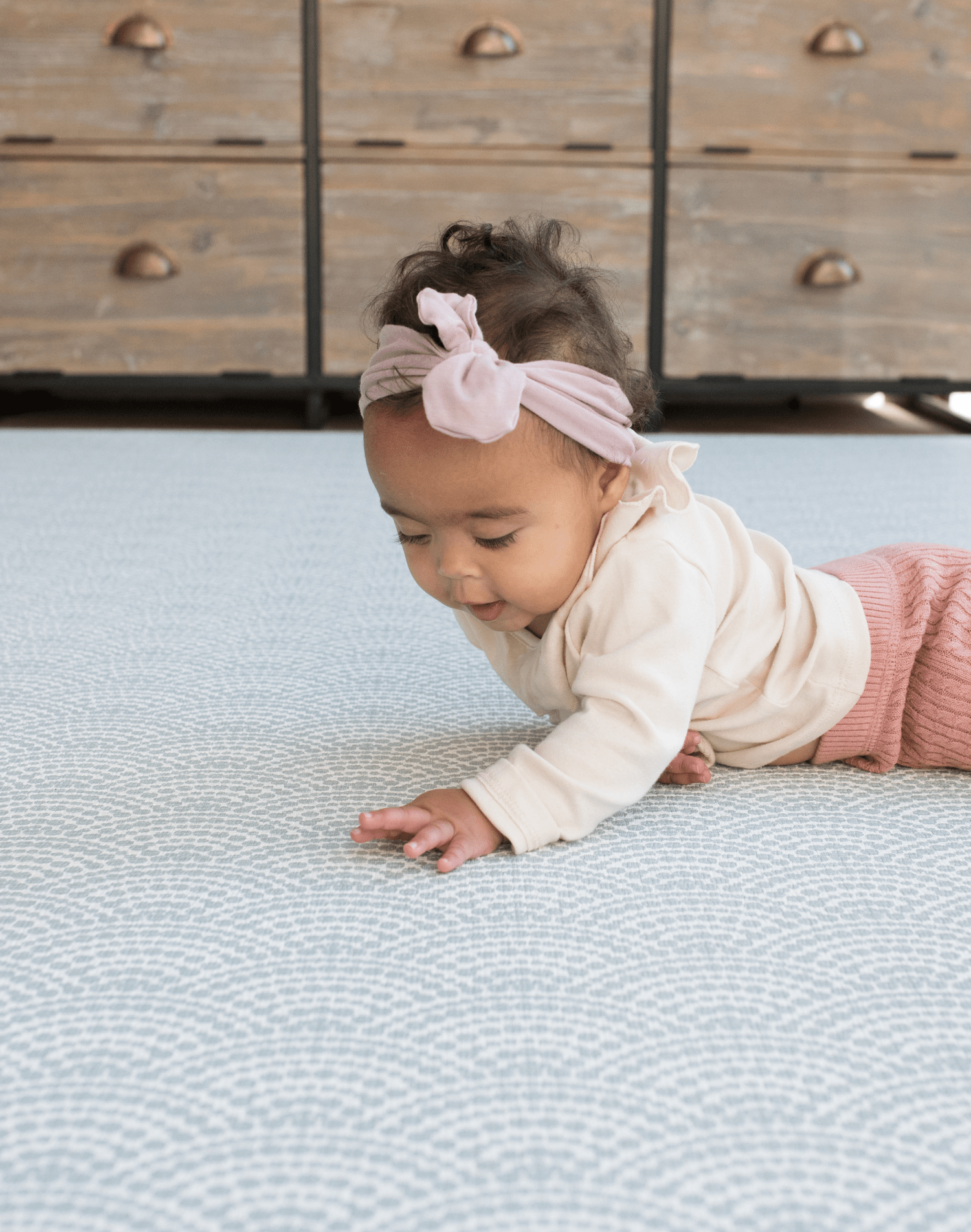 Baby with headband lays on protective play mat with modern scalloped design in gentle blue tones