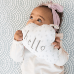 Baby resting on baby play mat with subtle scalloped pattern playing with soft toy
