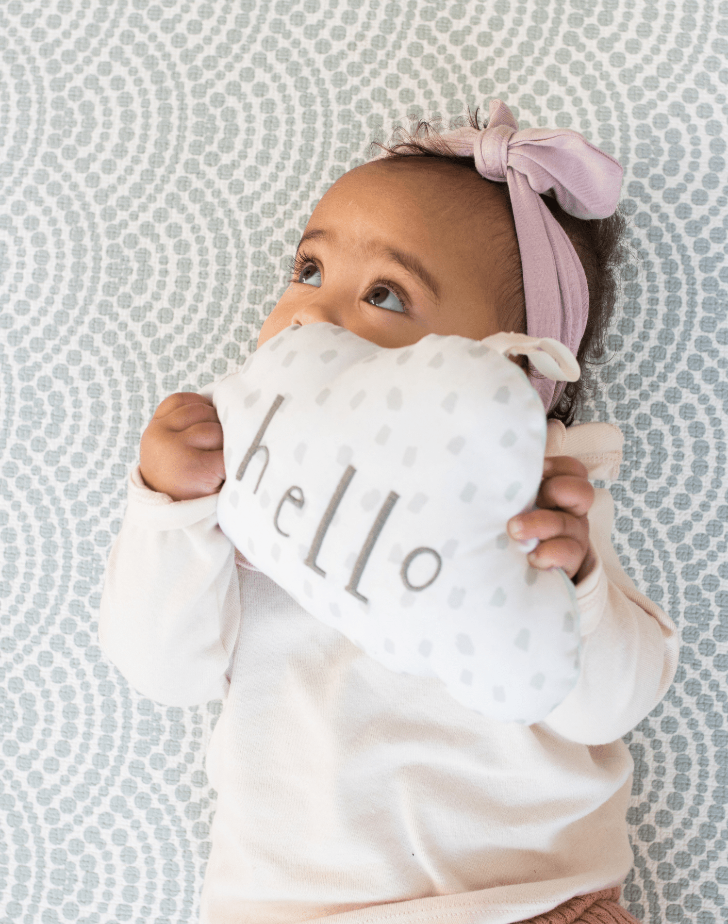 Baby resting on baby play mat with subtle scalloped pattern playing with soft toy