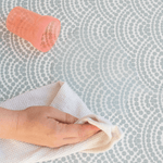 Hand wiping away water spill on washable play mat with soft cloth