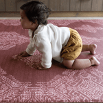 Baby crawls across large playing mat with thick memory foam to support joints and a textured surface for traction and support the red color complements boho kitchen styling