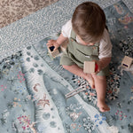Toddler plays on a Totter + Tumble woodland animal play mat with botanical patterns; a one-piece, non-toxic foam playmat perfect for modern nurseries.