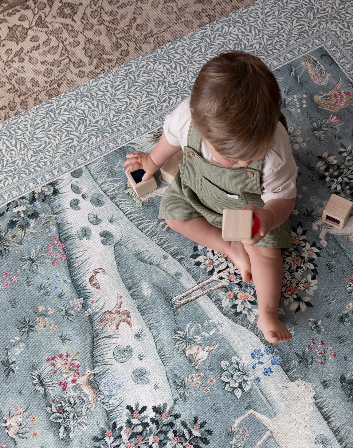 Toddler plays on a Totter + Tumble woodland animal play mat with botanical patterns; a one-piece, non-toxic foam playmat perfect for modern nurseries.