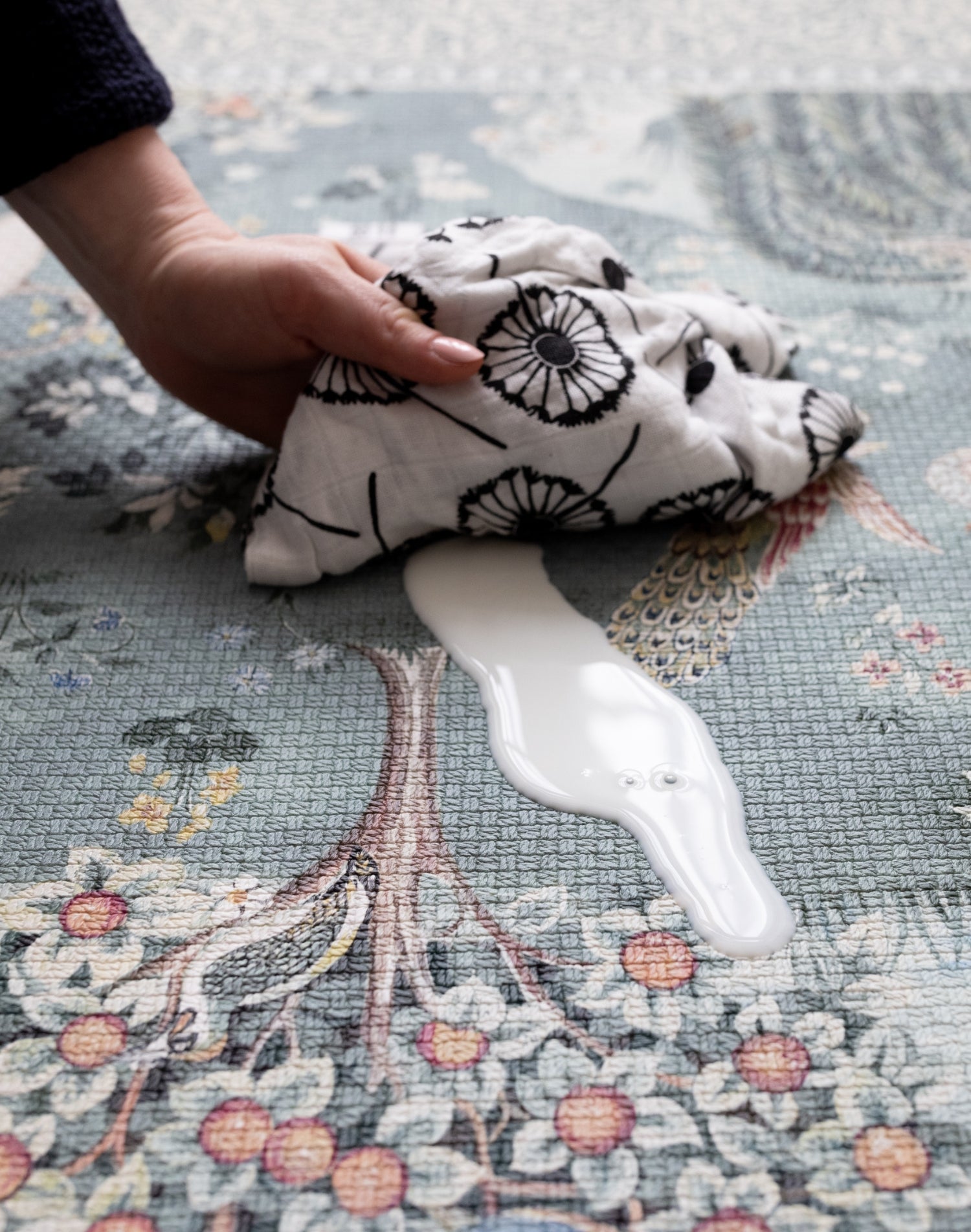 Wiping down a durable Totter + Tumble non-toxic foam play mat - easy-to-clean surface with William Morris floral heritage print in the Owl & Willow design, ideal for practical parenting with style.