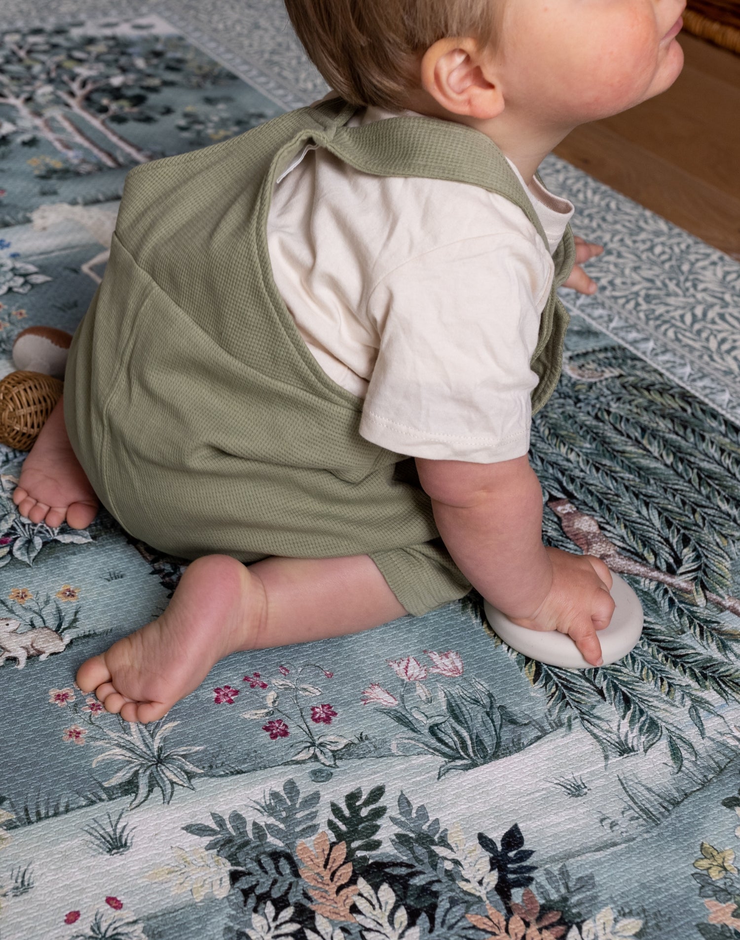 Side view of toddler exploring a decorative play mat with woodland and floral motifs - a premium foam mat for safe and chic play spaces.
