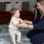 Parent supports toddler on a heritage-inspired playmat - a designer essential for family-friendly interiors and stylish parenting.