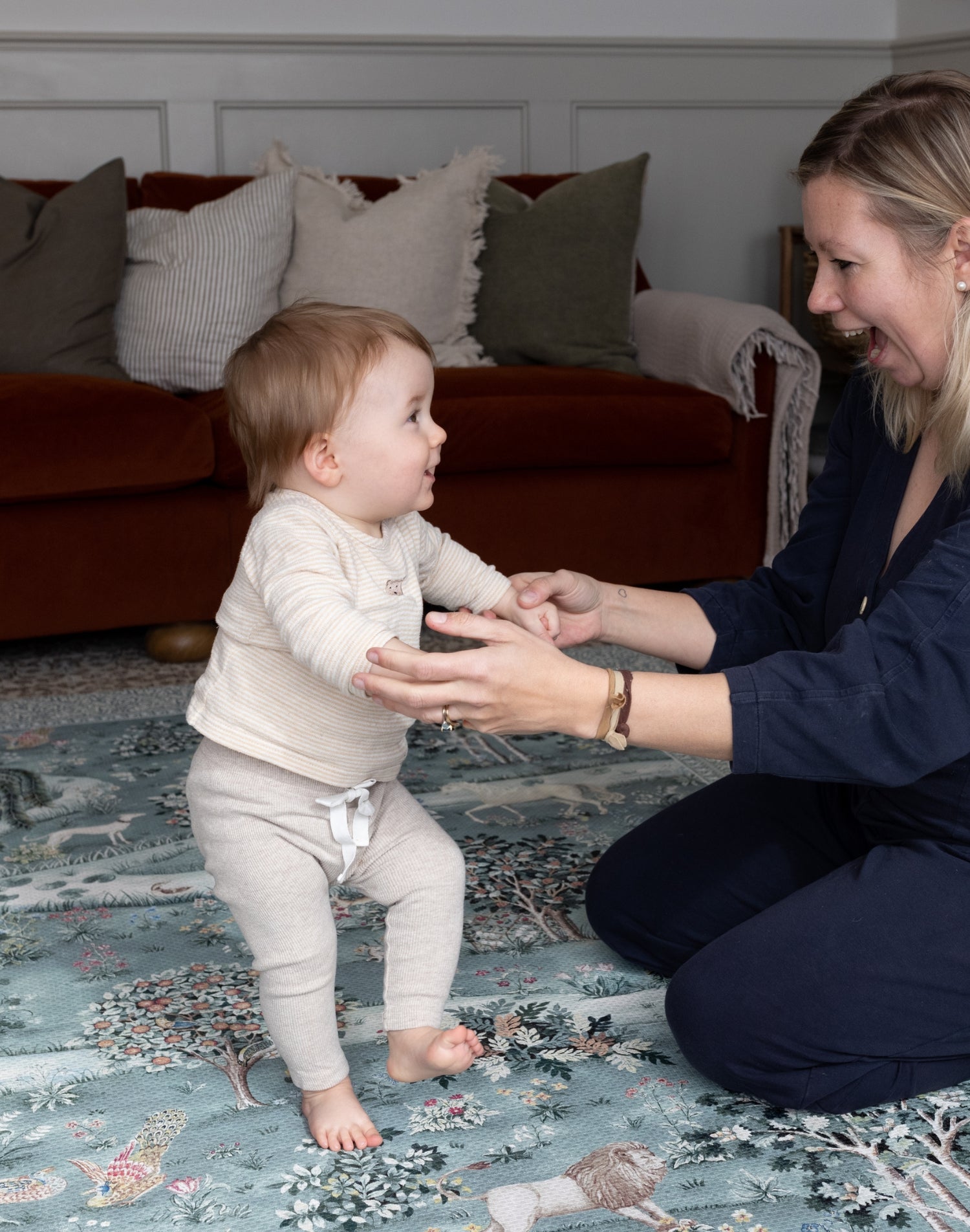 Parent supports toddler on a heritage-inspired playmat - a designer essential for family-friendly interiors and stylish parenting.