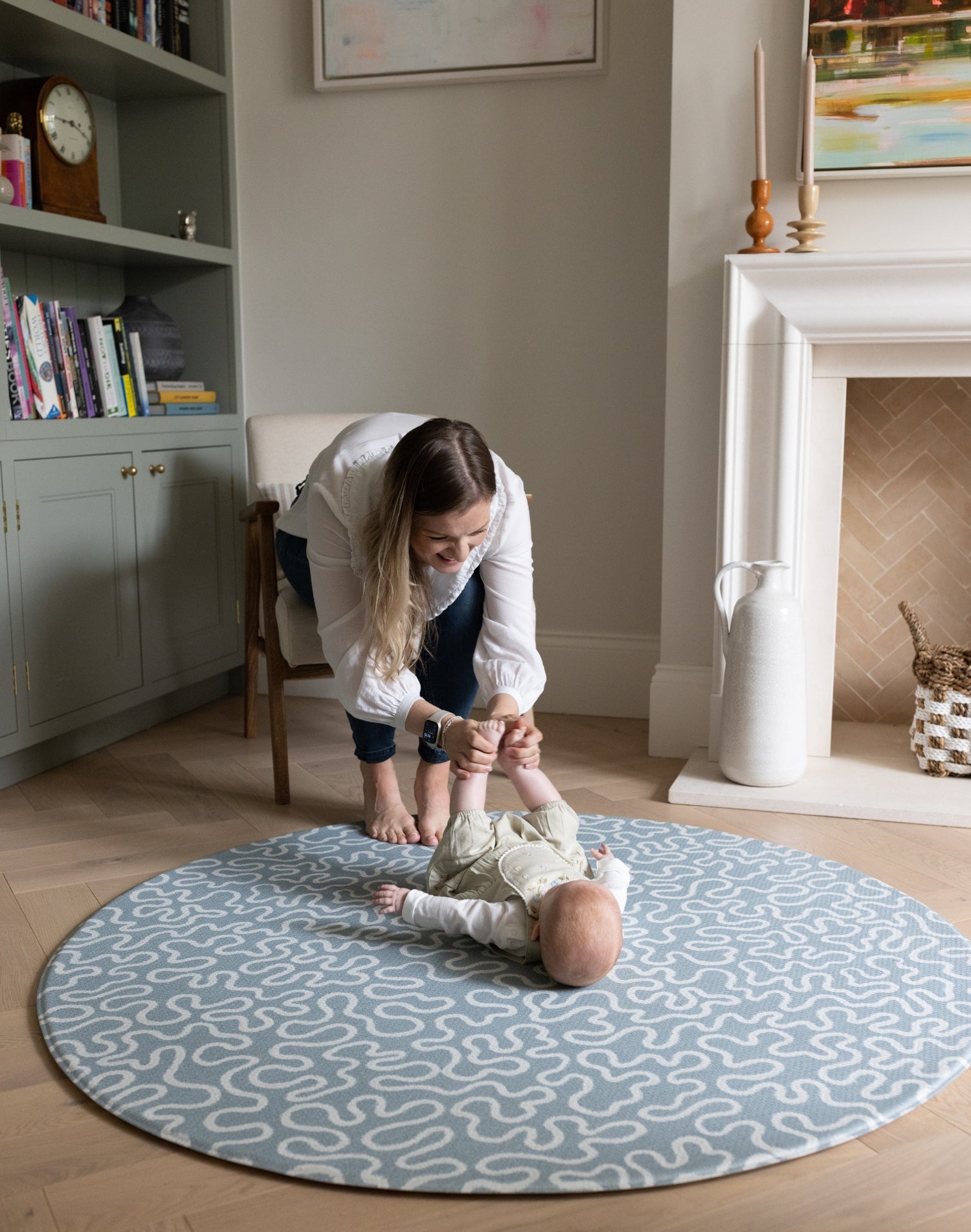 Mum playing with her baby on a patterned blue rug and round playmat in a home setting.