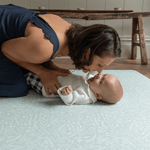 Mother kisses her little baby on the stylish green spielmatte by totter and tumble