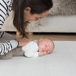 Mum rests gentle hand on the back of a baby laying on a supportive playmat with a gentle design ideal for modern spaces