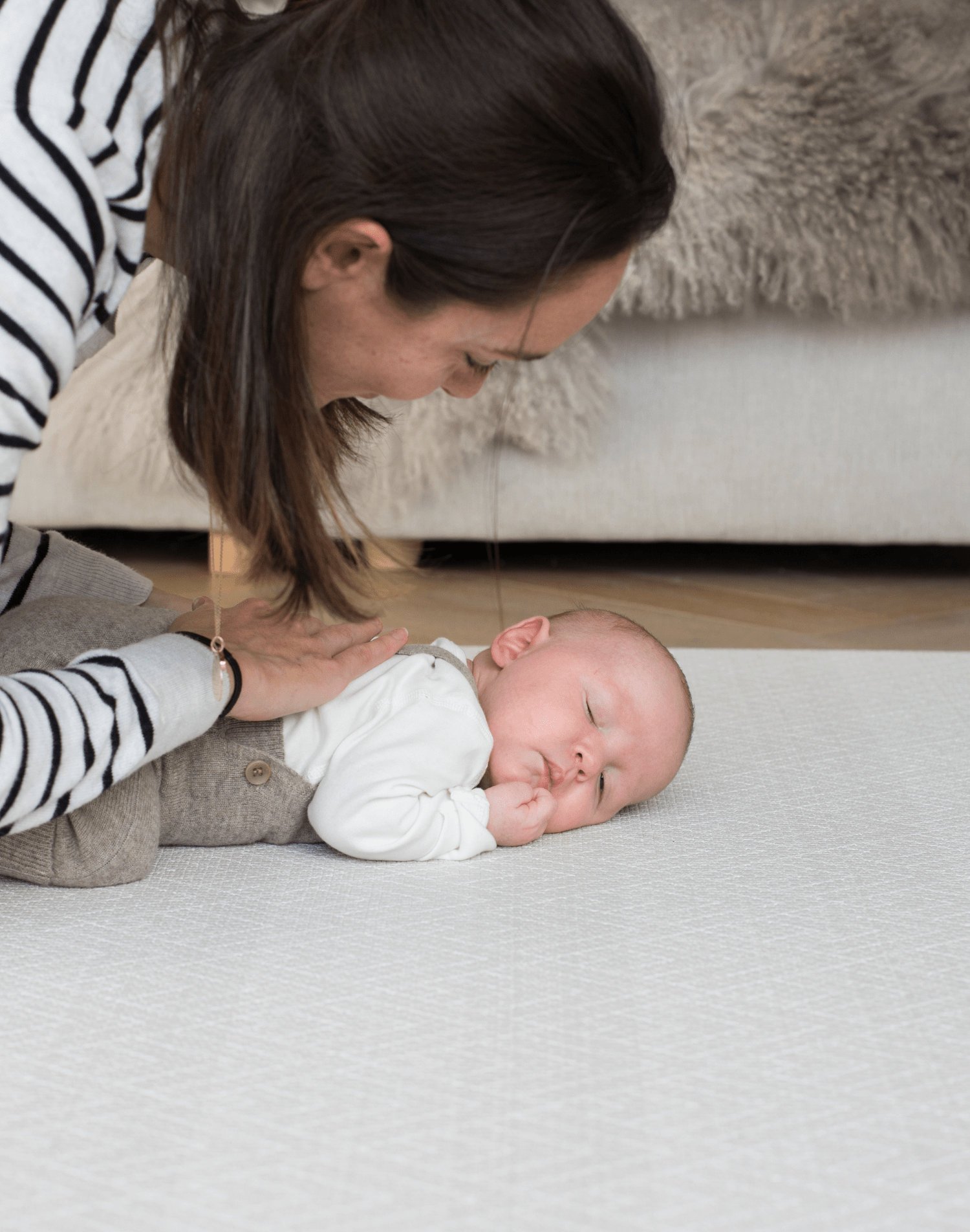 Mum rests gentle hand on the back of a baby laying on a supportive playmat with a gentle design ideal for modern spaces