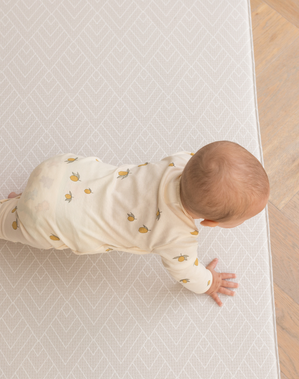 Baby crawling across neutral textured play mat that offers supports through the developmental stages 