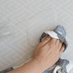 A hand is wiping up a water spillage using a muslin on the waterproof play mat that makes accidents easier