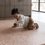 Baby crawling across the large tan play mat the rusa a textural animal print play mat design that looks beautiful in family home settings while providing the peace of mind floor time protection you need for your family