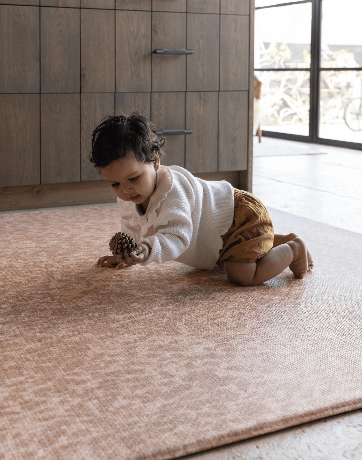 Baby crawling across the large tan play mat the rusa a textural animal print play mat design that looks beautiful in family home settings while providing the peace of mind floor time protection you need for your family