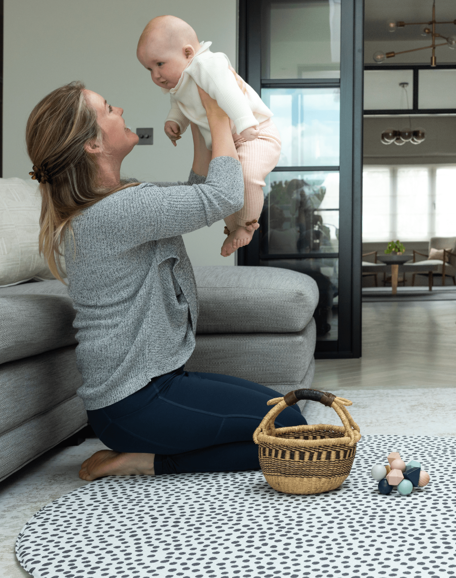 lady holds her baby while playing on the large round baby mat with a modern design