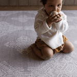 Baby kneels on grey play mat the sepi by totter and tumble a decorative design to complement modern interiors large size allows for crawling and exploring on the floor to support babies development
