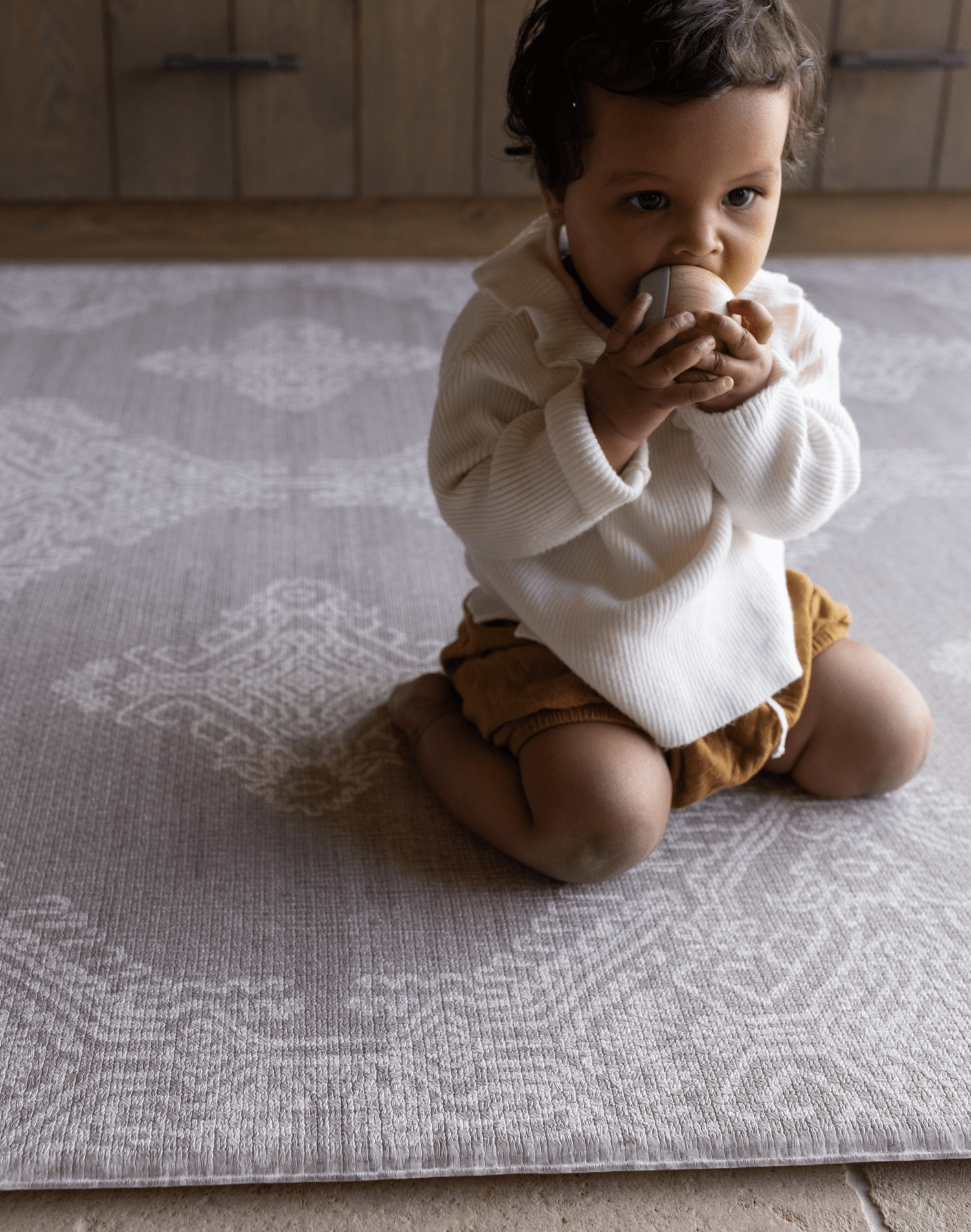 Baby kneels on grey play mat the sepi by totter and tumble a decorative design to complement modern interiors large size allows for crawling and exploring on the floor to support babies development