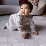 Baby girl crawls across the large grey crawling mat by totter and tumble the sepi designed to look like a rug with the practical features you need from a playmat a no compromise design perfect for modern family homes